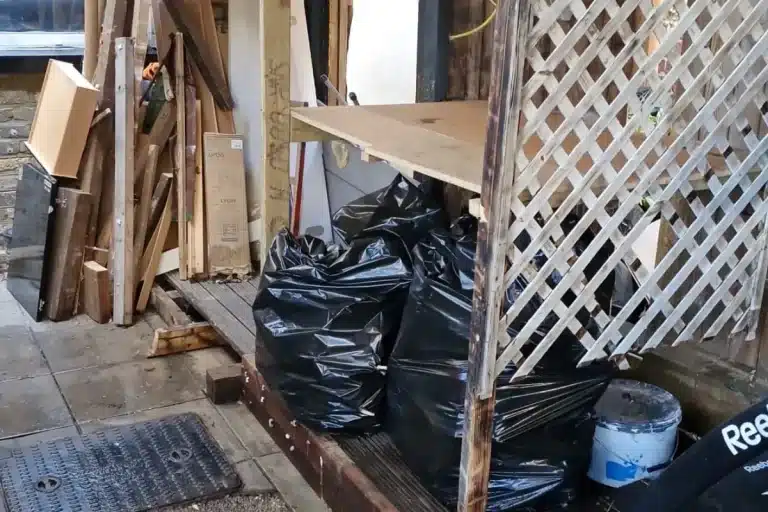 Old wood and rubbish bags by a garden fence, collected by a licensed carrier